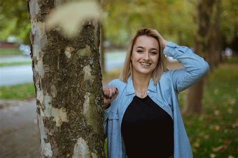 Premium Photo Smiling Caucasian Blonde Girl Leaning On The Tree In The Park