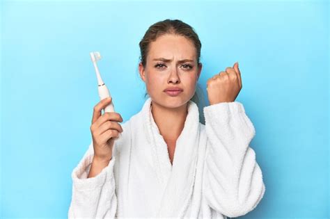 Premium Photo Blonde In Bathrobe With Electric Toothbrush In Studio Showing Fist To Camera