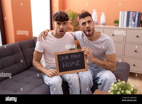 Homosexual Gay Couple Holding Blackboard With First Home Text In Shock Face Looking Skeptical