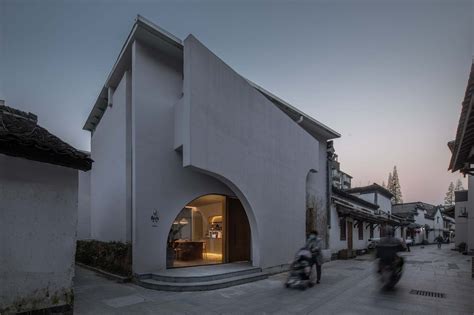 Two People Riding Bikes Past A White Building With Arched Doorways On