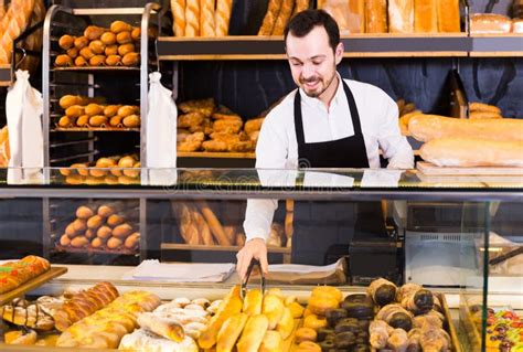 Male Shop Assistant Demonstrating Fresh Delicious Pastry In Bakery