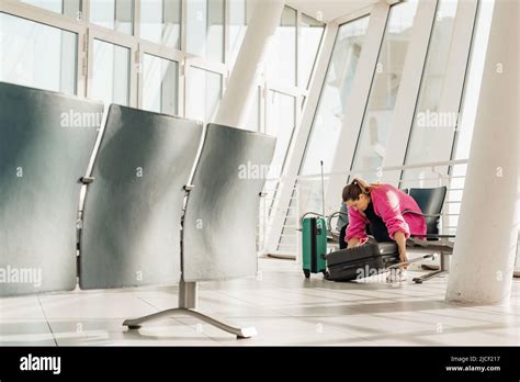 Passenger Sitting On Chair In Modern Light Airport With Panoramic Windows Opening Suitcase With