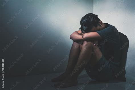 Young Depressed Asian Man Sitting Alone In Dark Room With Low Light