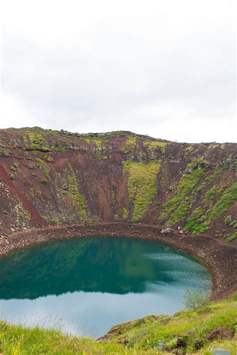 A Large Blue Lake Surrounded By Lush Green Hills And Grass On The Side