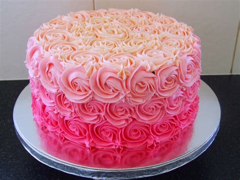 A Cake With Pink Frosting And Roses On It Sitting On Top Of A Table