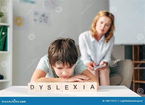 Centre D Enfant Triste Avec La Dyslexie Assis à La Table Avec Les Cubes En Bois Avec Marquer