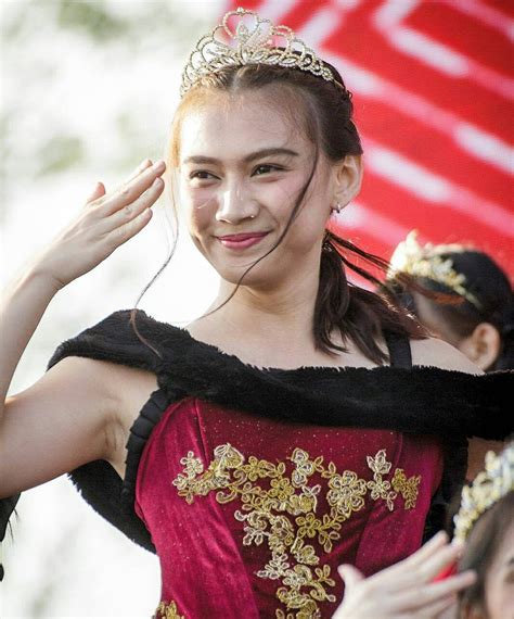 A Woman In A Red And Gold Dress Smiles As She Walks With Her Hands Behind Her Head