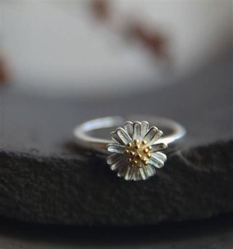 A Silver And Gold Ring With A Flower On The Middle Sitting On Top Of A