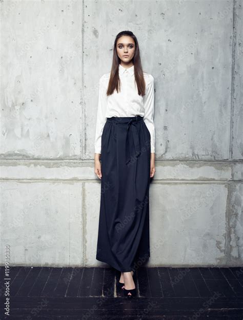 Fashion Model Wearing White Shirt And Long Black Skirt Posing In Studio