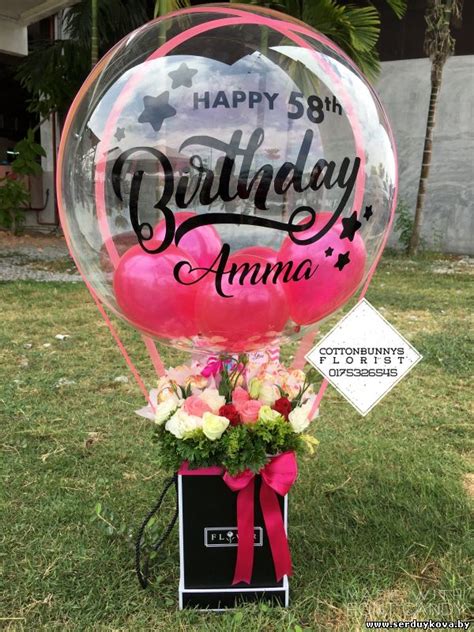 a birthday balloon sitting on top of a box filled with flowers and pink ...