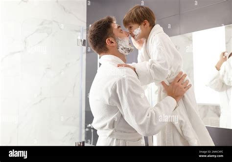 Dad And Son With Shaving Foam On Their Faces Having Fun In Bathroom