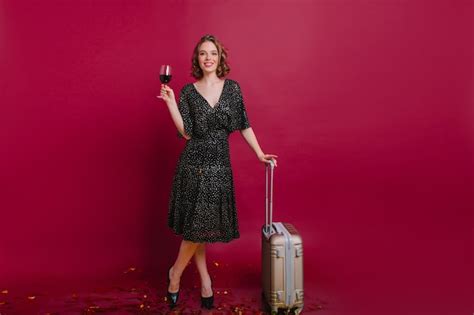 Photo pleine longueur d une femme blonde heureuse debout avec les jambes croisées et tenant une