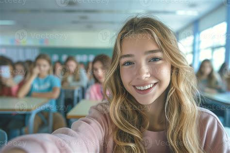 Smiling Teenage Girl With Long Blonde Hair Captures A Selfie In A Lively Classroom Filled With