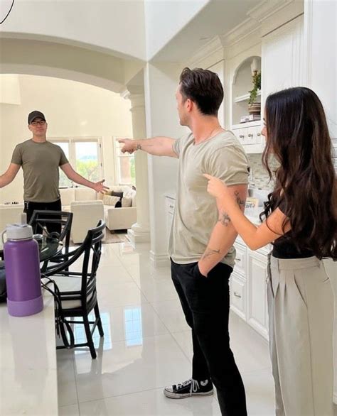 Two People Standing In A Kitchen Pointing At Something On The Counter