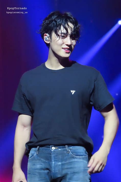 A Male In A Black T Shirt And Blue Jeans Is Standing On Stage With