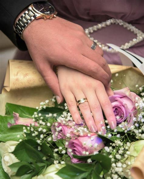 A Close Up Of A Persons Hands With Wedding Rings On Top Of Flowers