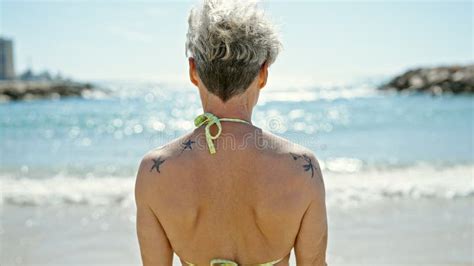 Middle Age Blonde Woman Tourist Wearing Bikini Standing Backwards At The Beach Stock Photo