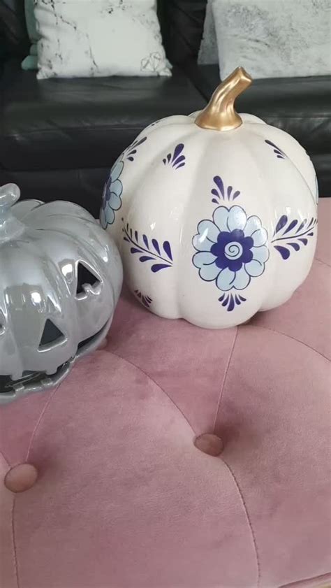 Two Ceramic Pumpkins Sitting On Top Of A Pink Velvet Ottoman Next To