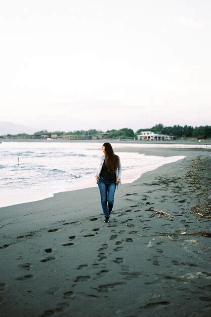 Premium Photo Young Woman Walks Along The Beach And Looks At The Surf