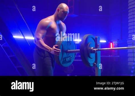 Muscular Male Bodybuilder With Naked Torso Stringing Round Black Weights Onto Barbell Man With