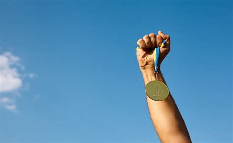 Mão de vencedor levantada e segurando a medalha de ouro fita contra