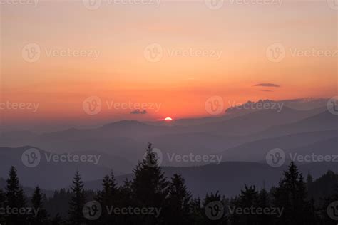 Fading sun hiding behind mountains, spruces silhouettes landscape photo