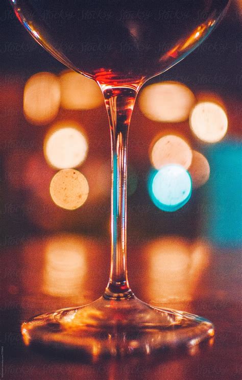 A Glass Of Wine Sitting On Top Of A Wooden Table Next To Blurry Lights