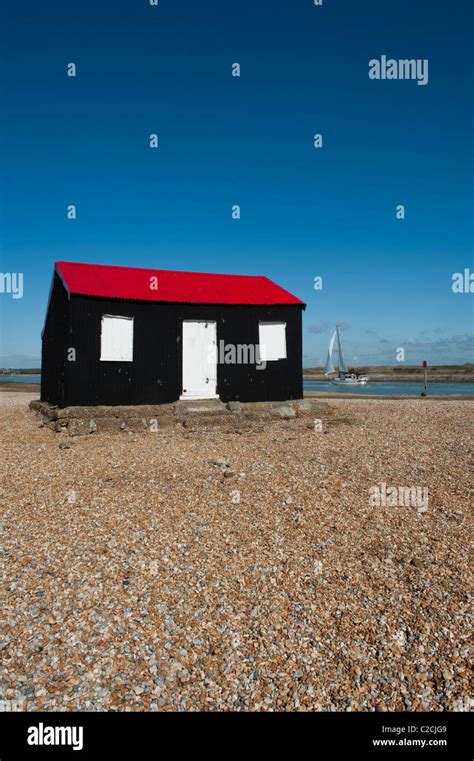 A White Yacht Sails Past A Red And Black Corrugated Hut With White