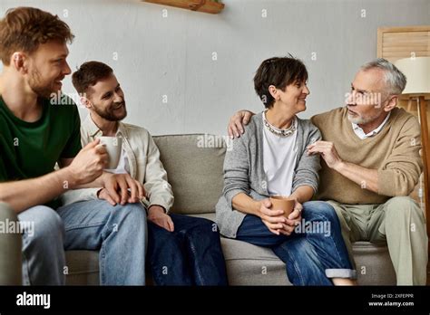 A Gay Couple Sits With Parents On A Couch Engaging In A Warm And