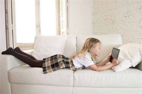 Petite Fille Blonde Se Trouvant Sur Le Divan à La Maison De Sofa Utilisant L Internet APP Sur La