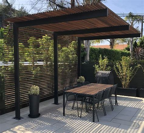 An Outdoor Dining Area With Wooden Slatted Walls And Black Metal Chairs