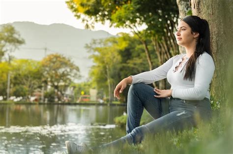Linda garota latina sentada à beira do lago admirando o pôr do sol dourado enquanto pensava em