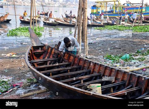 Worker Repairs A Wooden Boat Along The Banks Of The Buriganga River In