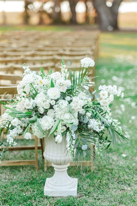 An Arrangement Of White Flowers And Greenery Sits In A Urn On The Grass