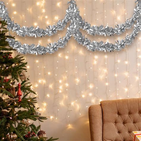 A Decorated Christmas Tree In Front Of A Wall With Purple Tinsel