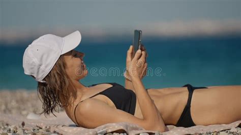 Relaxed Woman Tourist In Bikini Sunbathes On Sea Beach Close To Water