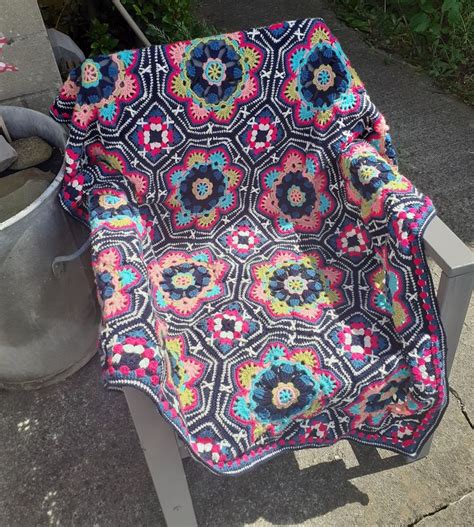 A Crocheted Blanket Sitting On Top Of A Wooden Bench