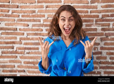 Beautiful Brunette Woman Standing Over Bricks Wall Shouting With Crazy Expression Doing Rock