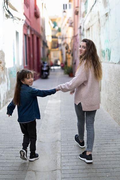 Premium Photo Rear View Of Sisters Holding Hands While Walking In Alley