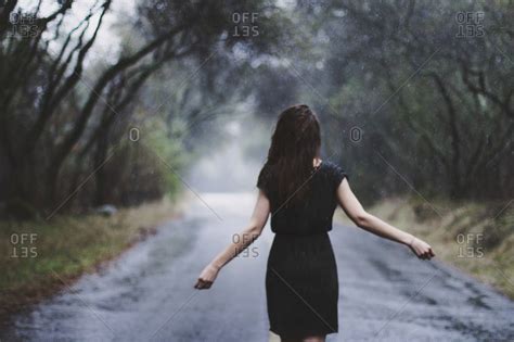 Woman walking in rain along country road stock photo - OFFSET