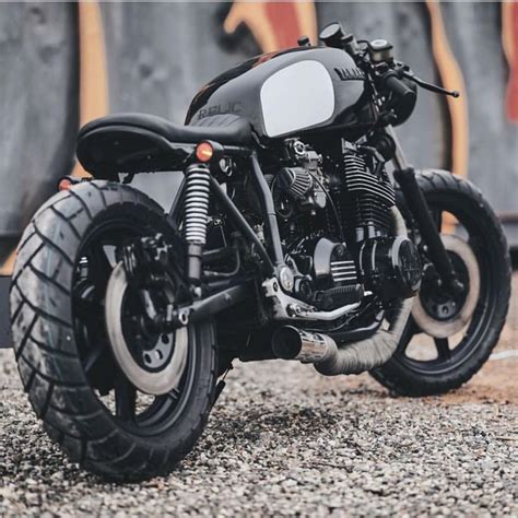 A Black Motorcycle Parked On Top Of A Gravel Road Next To Graffiti