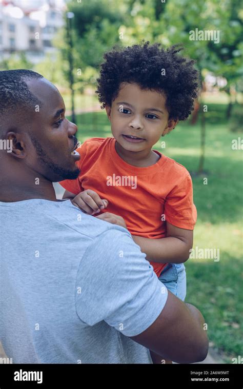 Young African American Man Holding Adorable Son While Walking In Park