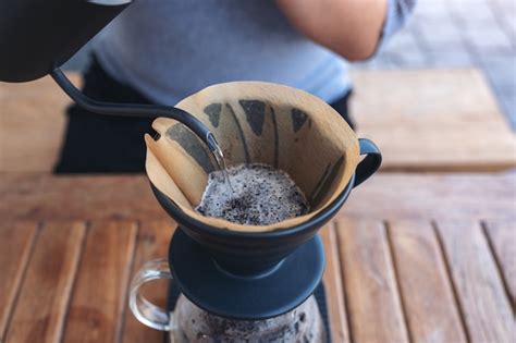 Mão de uma mulher despejando água quente para fazer café em uma mesa de