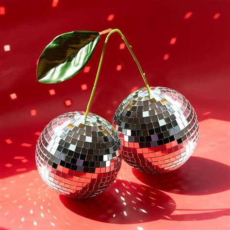 Two Shiny Disco Balls Sitting On Top Of A Red Surface Next To A Green Leaf