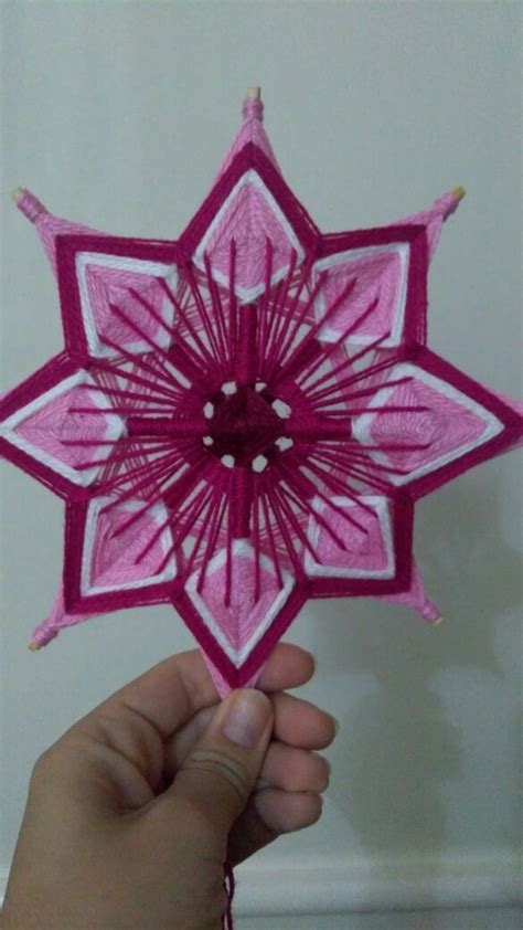 A Hand Holding Up A Pink And White Ornament With Red Thread On It