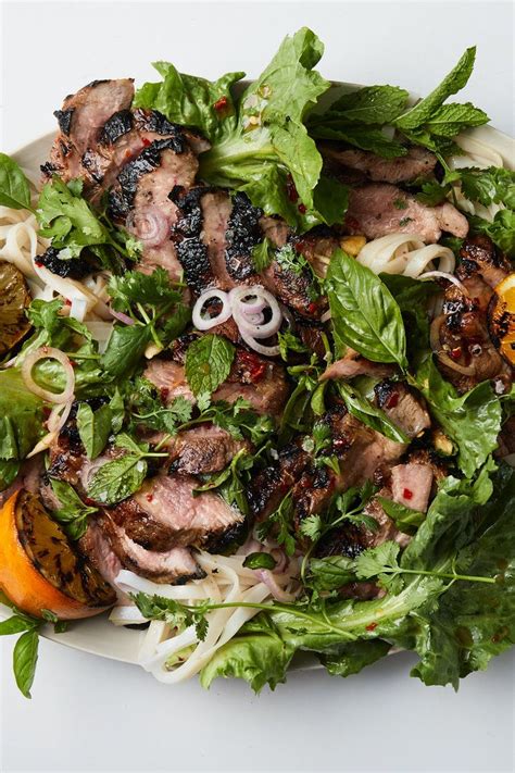 A White Plate Topped With Meat And Veggies Next To Lemons On A Table