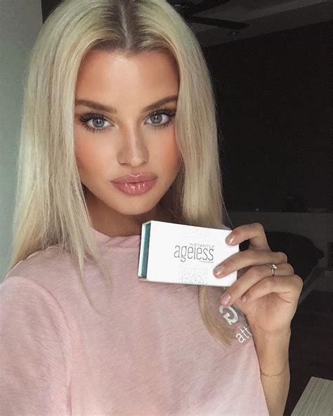 A Woman With Blonde Hair And Blue Eyes Holding Up A Box Of Ageless Products