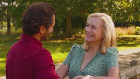 Smiling Mature Mother With Mixed Race Adult Son Leaning On Wooden Fence On Walk In Summer