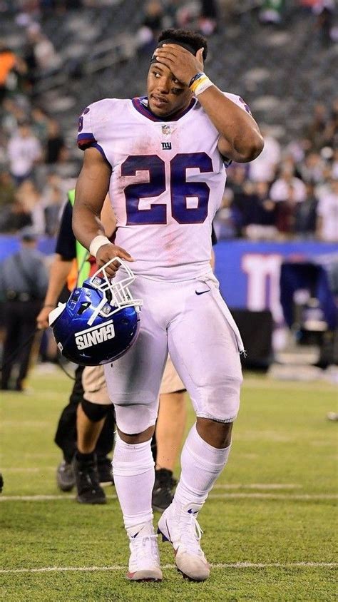 A Football Player Is Walking On The Field With His Helmet In One Hand