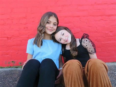 Two Girls Sitting Next To Each Other In Front Of A Red Wall